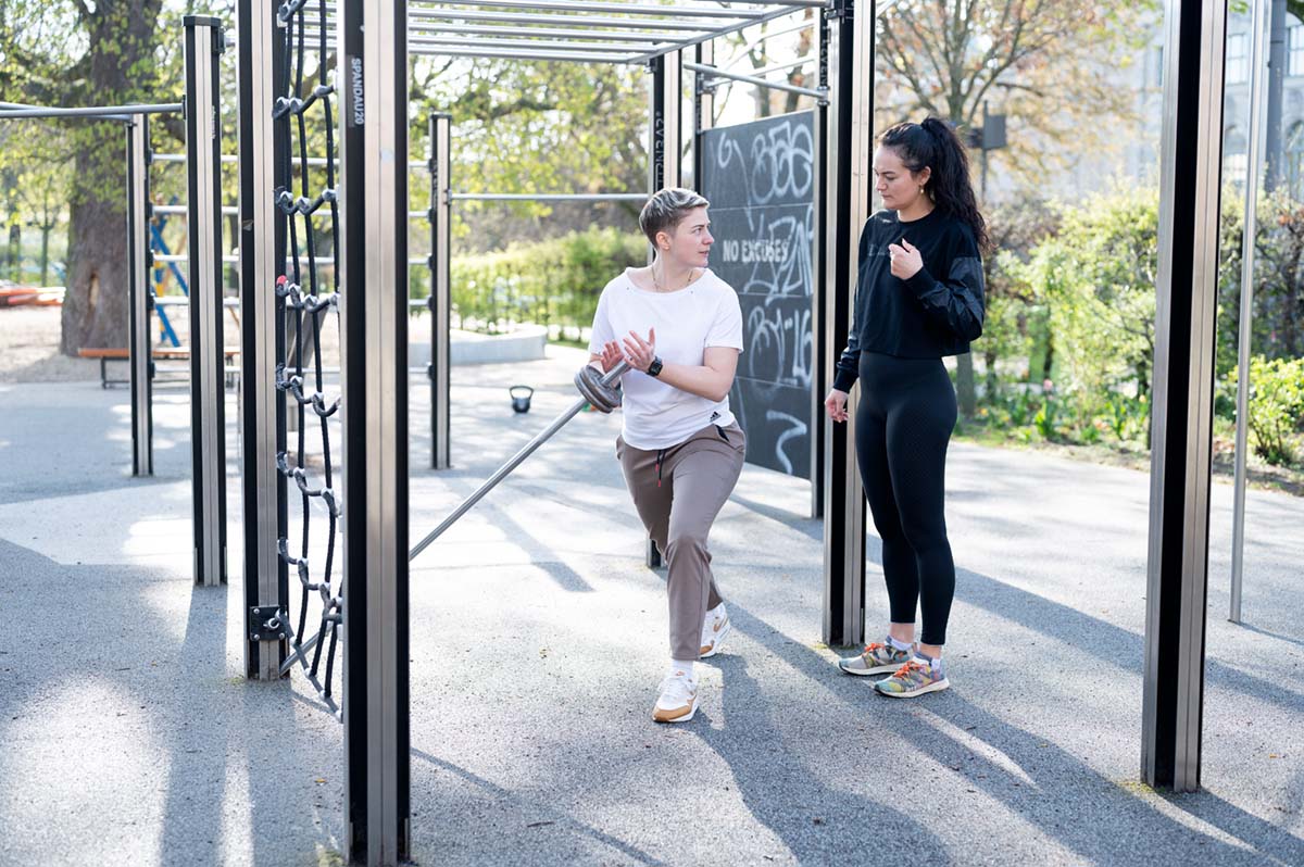 Coach Anna demonstriert einer Athletin die Technik für eine Langhantelübung, Schwerpunkt auf Kraft und Technik.