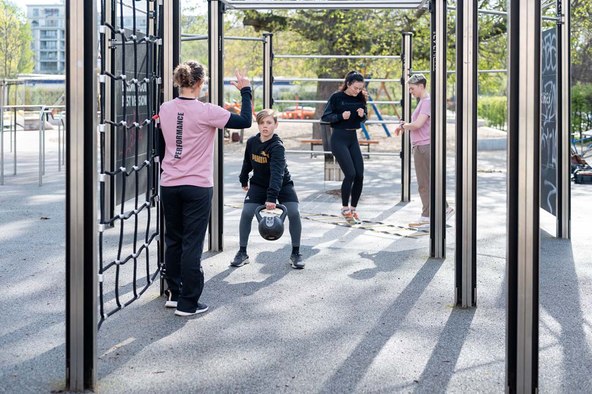 Coach Bibiane und Coach Anna leiten. Ein Training mit zwei Athlet:innen im Calisthenics Park, Fokus auf Koordination und Kraftausdauer.